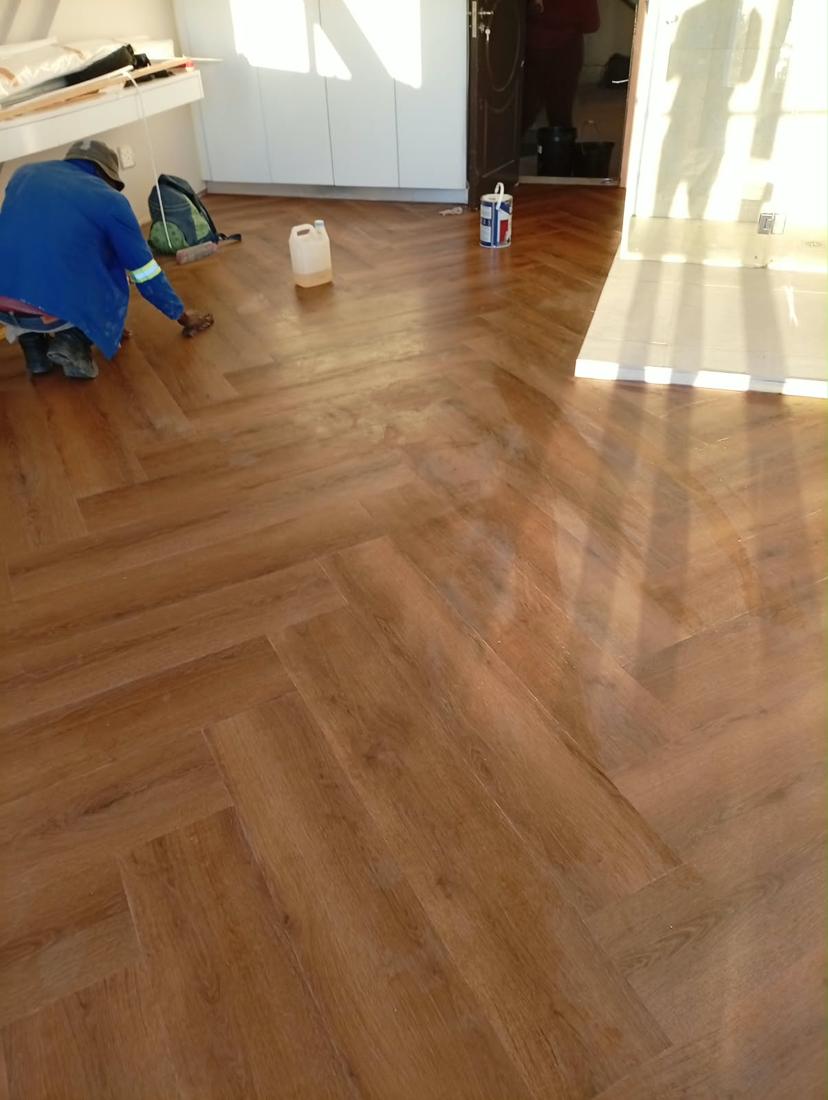 A finished herringbone laminate floor beside a doorway, tools left on the floor at the end of the job