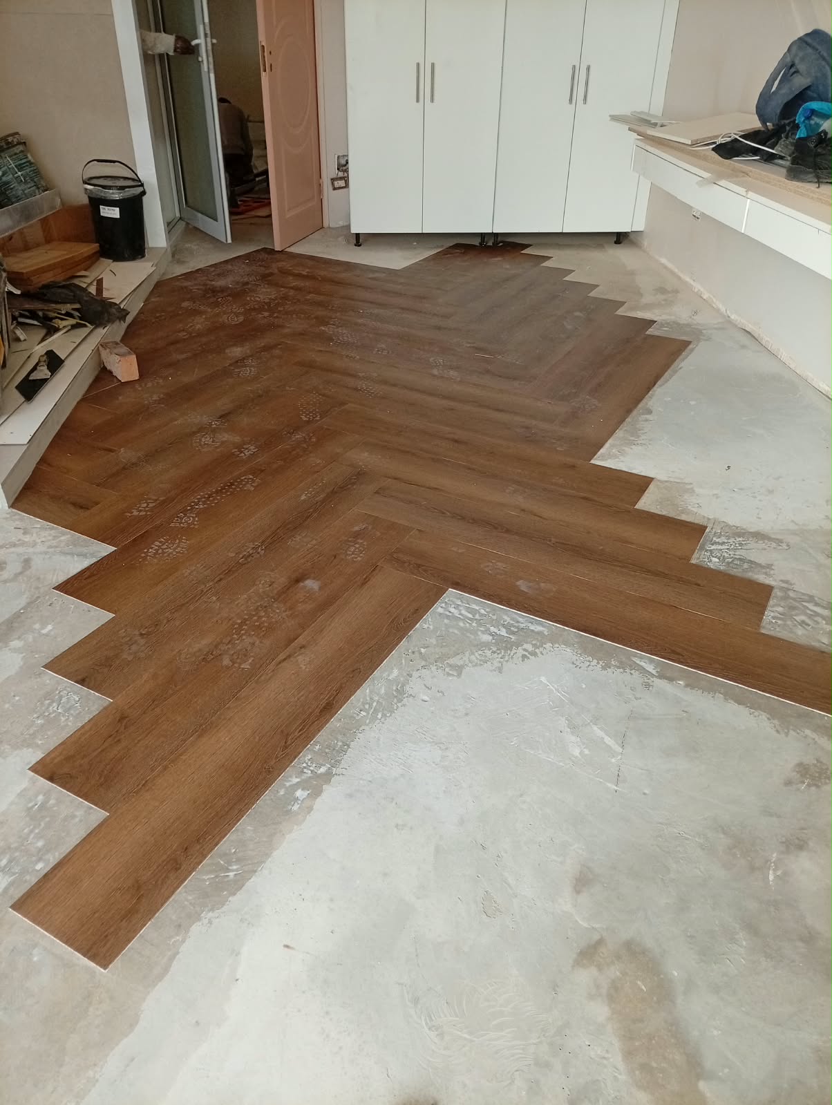 Herringbone laminate flooring mid-install, boxes of planks and tools laid out on the floor