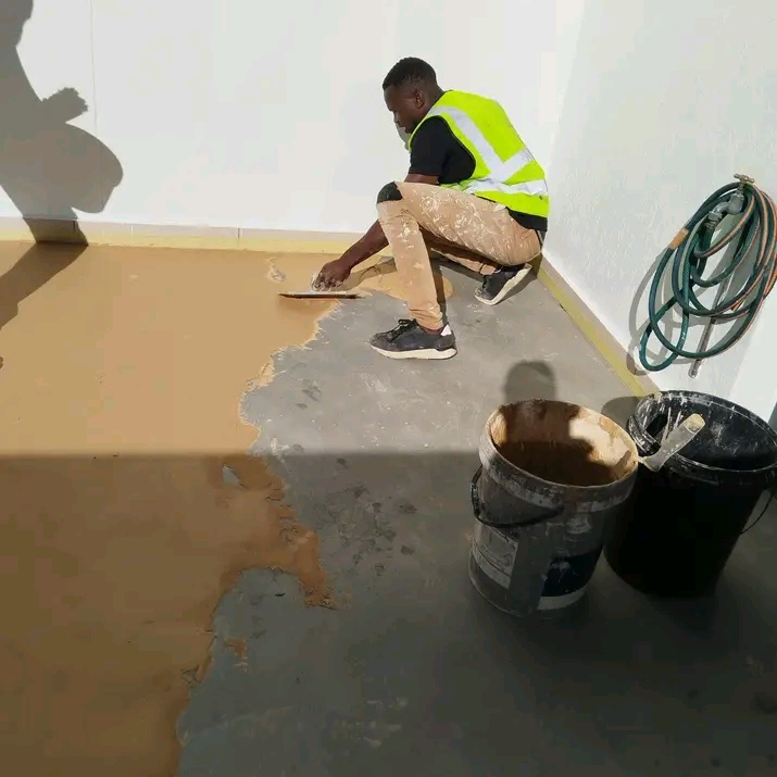 A worker applying a yellow waterproofing coating to a floor before flooring or tiling goes down