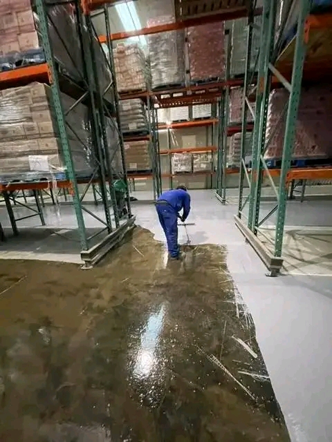 An epoxy floor coating being spread across a warehouse floor between rows of pallet racking