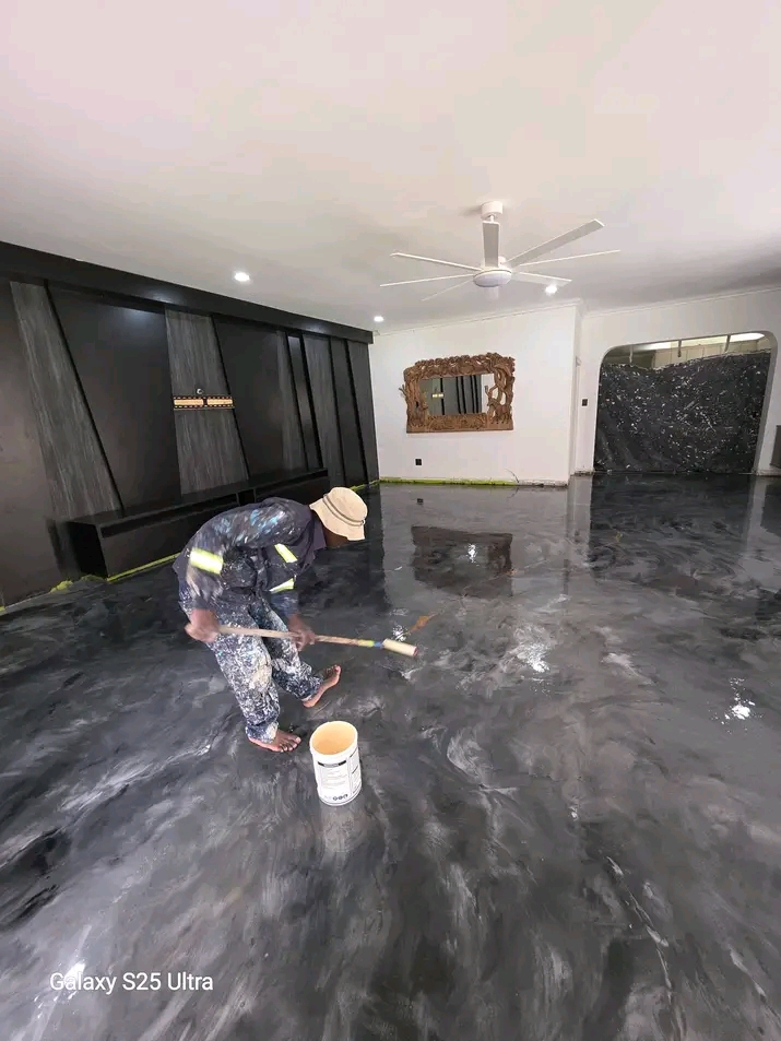 A metallic resin floor being applied by hand in a renovated living room with a dark feature wall and ceiling fan
