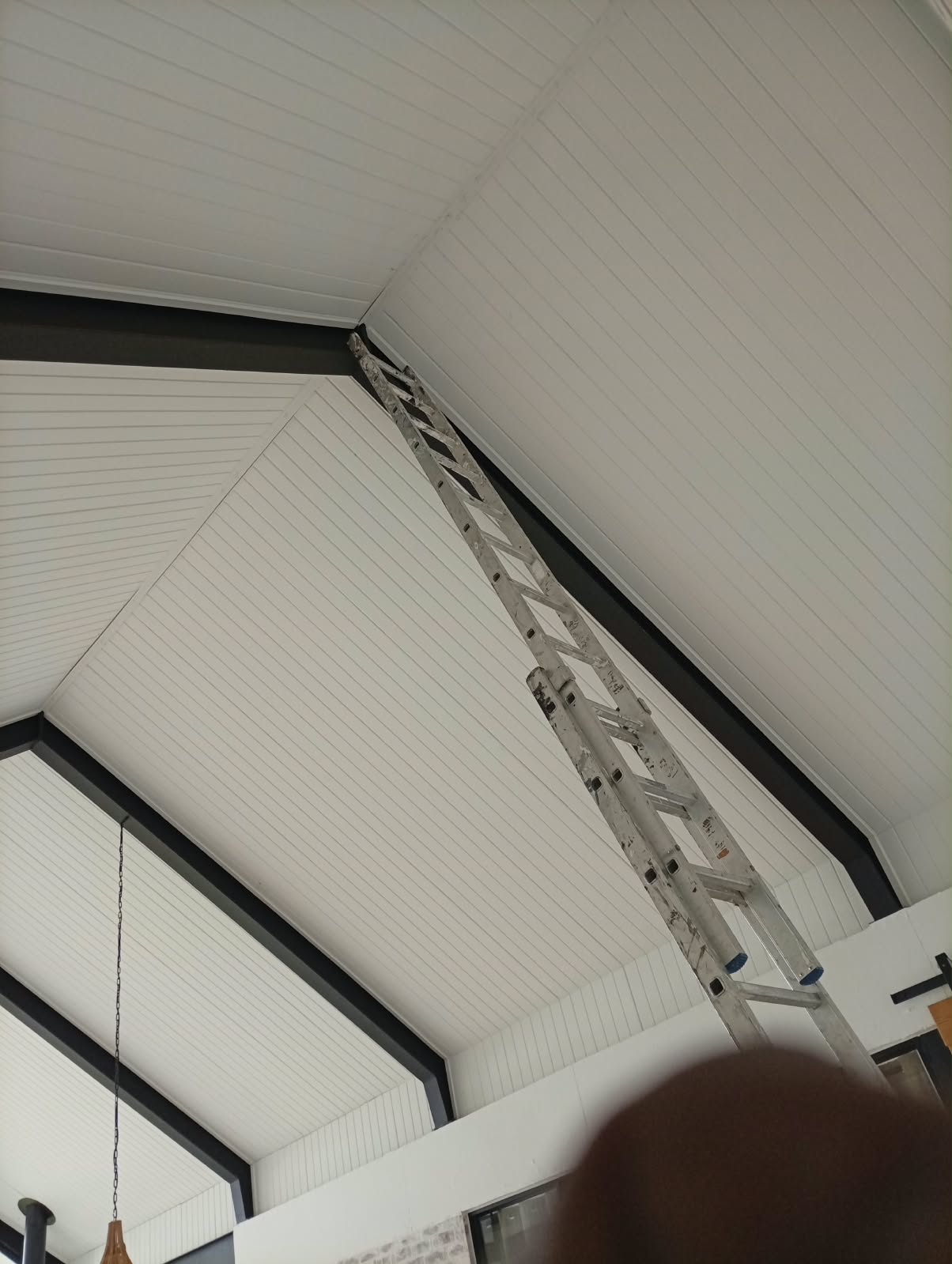 Looking up at a vaulted ceiling and steel beams during a double-volume renovation, a ladder reaching the mezzanine